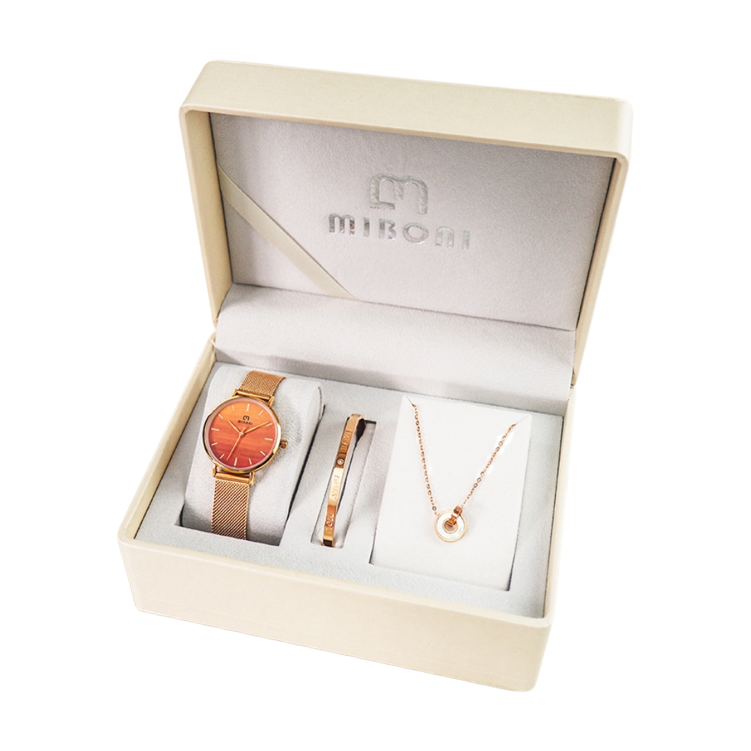 A Mibom jewelry gift set displayed inside an open cream-colored presentation box. The set includes a rose gold mesh-band watch with a round orange dial, a slim rose gold bracelet, and a delicate rose gold necklace with a white circular pendant, all arranged on white display cards.