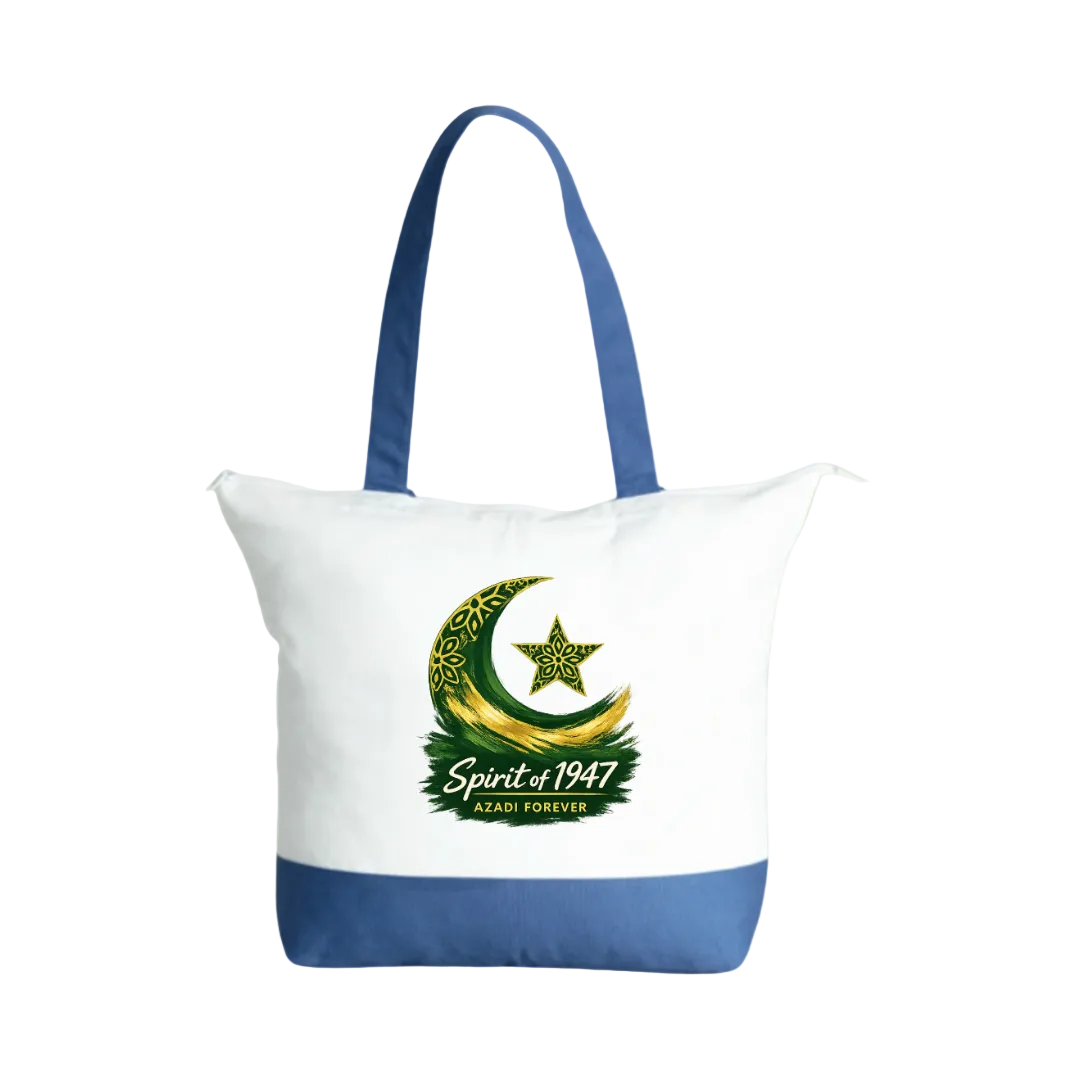 A white canvas tote bag with blue handles and a blue bottom panel, featuring a green and gold crescent moon and star graphic with the text 'Spirit of 1947' and 'AZADI FOREVER' on the front, set against a solid light green background.