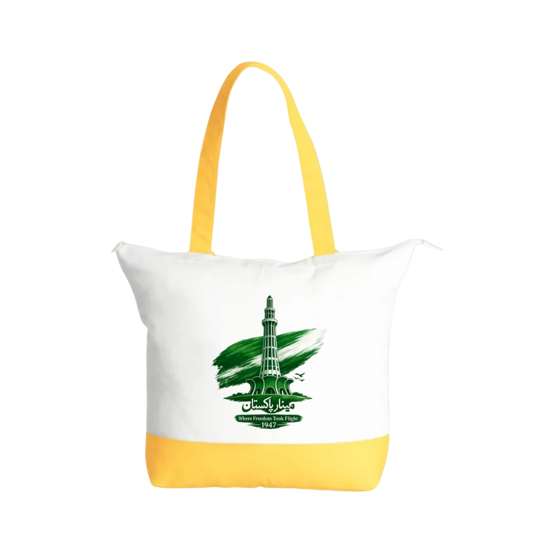 A white canvas tote bag with bright yellow handles and a yellow bottom band, featuring a green graphic of a tower and the flag of Iraq on the front, set against a solid light green background.